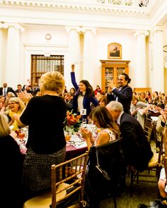 a large group of people sitting at tables in a room with white walls and ceilings