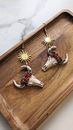 two cow heads with flowers and sunbursts hanging from them on a wooden tray