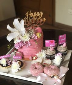 a pink birthday cake surrounded by cupcakes and flowers