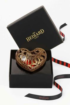 a heart shaped brooch in a black box with red and white ribbon around it