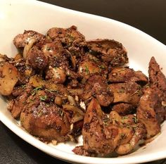 a white bowl filled with cooked meat and vegetables on top of a black countertop