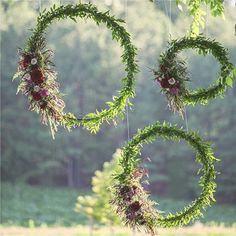 an arrangement of flowers and greenery hanging from the ceiling in front of some trees