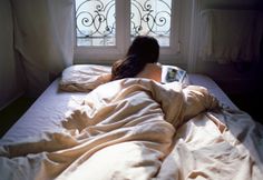 a woman laying in bed reading a book by a window with iron bars on the windowsill