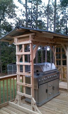 an outdoor bbq on a deck with a grill in the middle and trees behind it