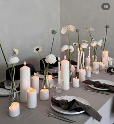 the table is set with white candles and flowers in vases, plates and napkins