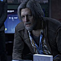 a man with grey hair and beard sitting in front of a laptop computer next to another person