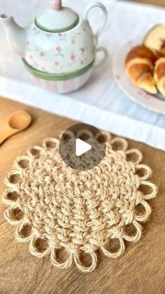 crocheted doily on wooden table next to tea pot and plate with pastries