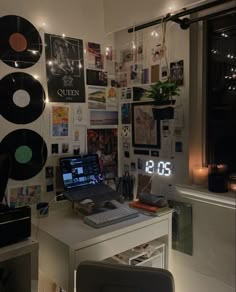 a laptop computer sitting on top of a desk next to a wall covered in records