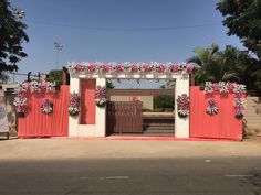 a red and white gate with pink flowers on it's sides, in front of a building