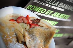 a crepe with strawberries and powdered sugar sits on a plate next to a menu