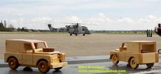 two wooden toy cars sitting on top of an airport tarmac with a helicopter in the background