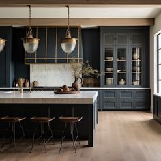 a kitchen with dark blue cabinets and wooden floors, two pendant lights hanging over the island