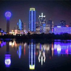 the city skyline is lit up in blue and white lights at night, reflecting on the water