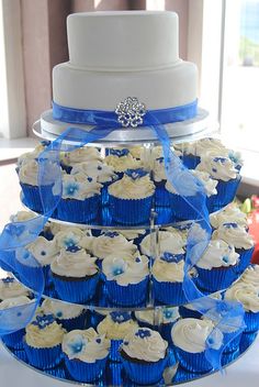 a tiered cake with cupcakes on the bottom and blue ribbon around it