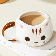 a cat shaped coffee mug sitting on top of a book next to a cup of coffee