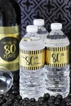 three bottles of bottled water sitting next to some blueberries on a table with black and gold decorations