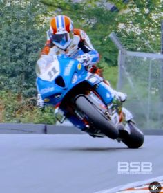 a man riding on the back of a blue motorcycle down a race track with trees in the background