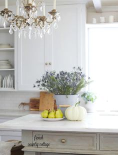 a chandelier hanging from the ceiling above a white kitchen island with fruit and vegetables on it