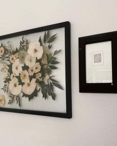 two framed pictures hanging on the wall with flowers in them and one has a black frame