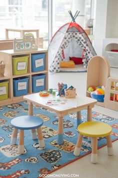 Bright and colorful children's playroom featuring a small table with art supplies, two stools, a toy storage unit with labeled bins, and a cozy play tent in the background. Play Area In Living Room, Living Room Setups, Montessori Bedroom, Small Nurseries