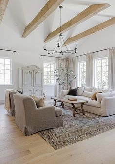 a living room filled with white furniture and wooden beams on top of the ceiling,