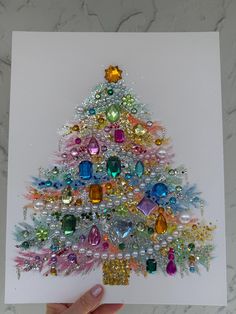 a hand holding up a card with a christmas tree made out of beads and jewels