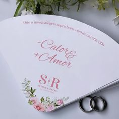 two wedding rings sitting on top of a white paper with flowers and greenery in the background