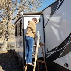 a woman standing on a ladder next to a white and black trailer