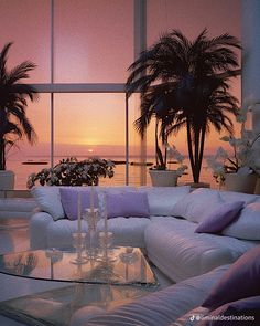 a living room filled with white furniture and palm trees in the window sill at sunset