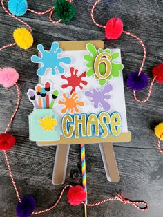 an easel with the word chase painted on it, surrounded by pom - poms