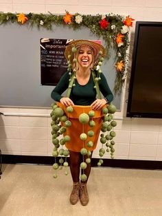 a woman wearing a hat and holding a bucket full of green fruit in front of a bulletin board