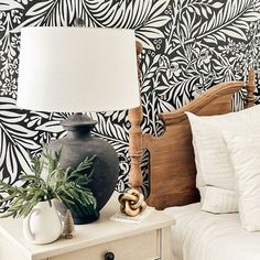 a lamp on a nightstand next to a bed with a black and white wallpaper