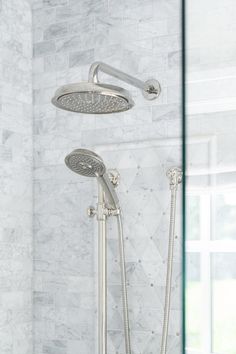 a shower head and hand shower in a white tiled bathroom with marble tiles on the walls