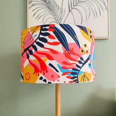 a colorful lamp shade on a wooden table next to a painting and plant in a green room