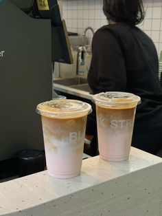 two coffee cups sitting on top of a counter next to a woman in a black shirt