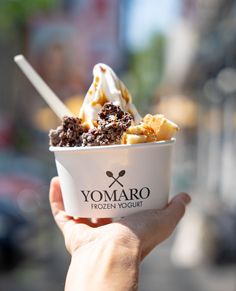 a person holding up a bowl of ice cream with toppings in it on the street