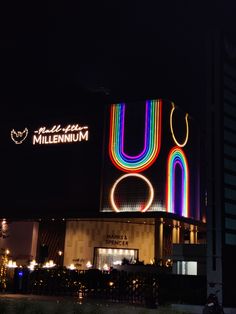 the neon sign is lit up in front of a large building with a circular design on it's side