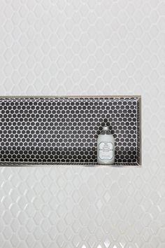 a white and black tiled wall with a metal grate in the middle that has a bottle on it