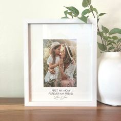 a white vase sitting on top of a wooden table next to a framed photo and a plant