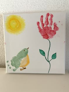 a painting on a white surface with a bird and handprinted flower next to it