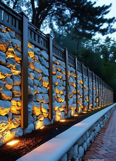 a stone wall with lights on it next to a brick walkway and trees in the background