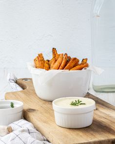 a wooden table topped with white bowls filled with food next to a bowl of dip