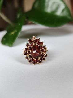 A large, bold and substantial garnet ring modelled in 10k yellow gold. The centre pear dhaped garnet appears to be rose cut, measuring approximately 9x6mm. It is surrounded by double halos consisted of smaller round cut garnets. The end result is this stunningly large centre pear shape measuring 20x17mm! The weight of this ring is also impressive (7.92g). It is stamped 10k with its maker's mark on the inside of the band, though the markings are a bit worn out. It has been tested to confirm 10k c Double Halo, Garnet Gemstone, Garnet Rings, Pear Shaped, Cocktail Rings, Rose Cut, Makers Mark, Pear, Garnet