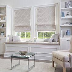 a living room filled with white furniture and windows covered in roman blind shades on the windowsill