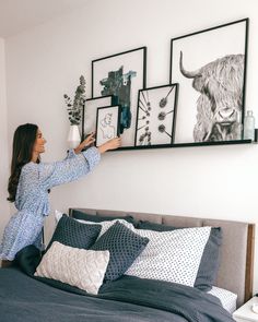 a woman is holding up pictures on the wall above her bed