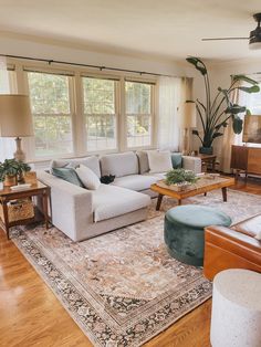 a living room filled with lots of furniture and large window covered in plants on top of a hard wood floor