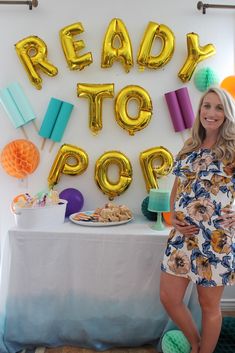 a woman standing in front of a table with balloons and decorations on it, reading to pop