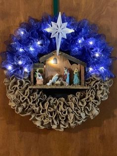 a nativity wreath with blue lights and a star hanging from the top on a door