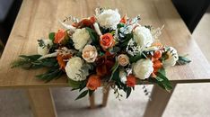 an arrangement of flowers is sitting on a wooden table with white and orange flowers in the center