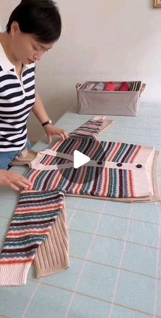 a woman sitting at a table working on some knitted items